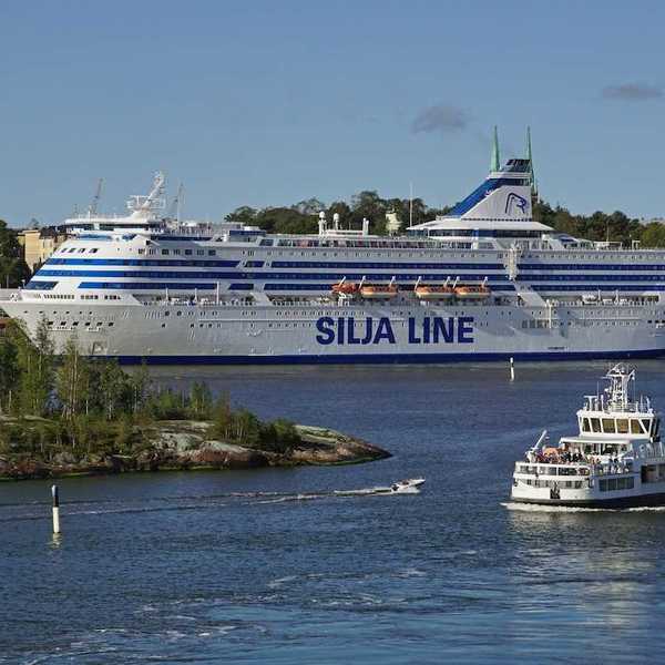 View of Helsinki harbor on a summer day with the Suomenlinna fortress ferry in the front and a large ferry ship behind it.