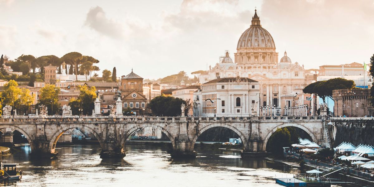View of the Vatican dome in Rome with a bridge and river in foreground.