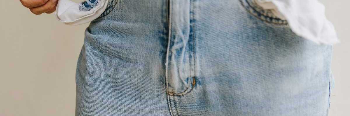 Waist-down shot of person retrieving a single coin from inside-out pockets of worn blue jeans