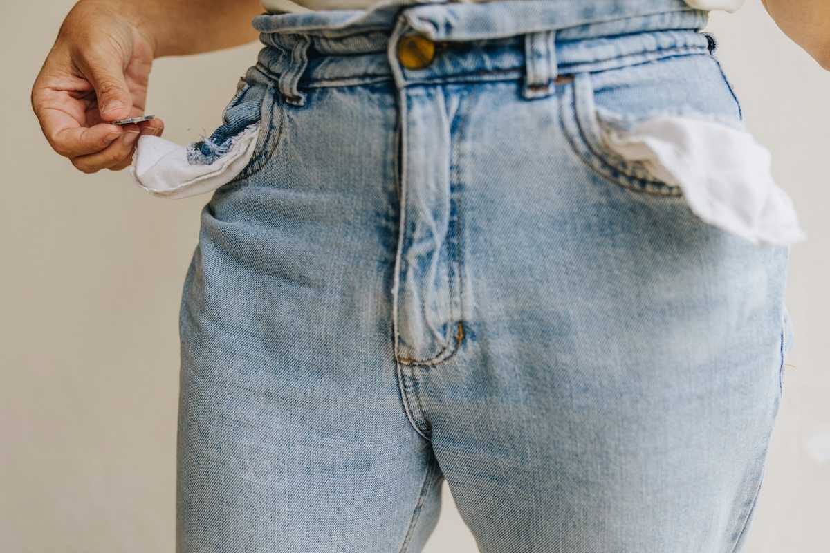 Waist-down shot of person retrieving a single coin from inside-out pockets of worn blue jeans