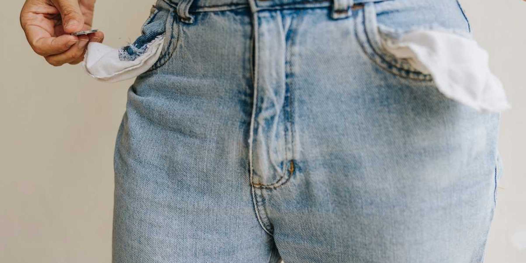 Waist-down shot of person retrieving a single coin from inside-out pockets of worn blue jeans