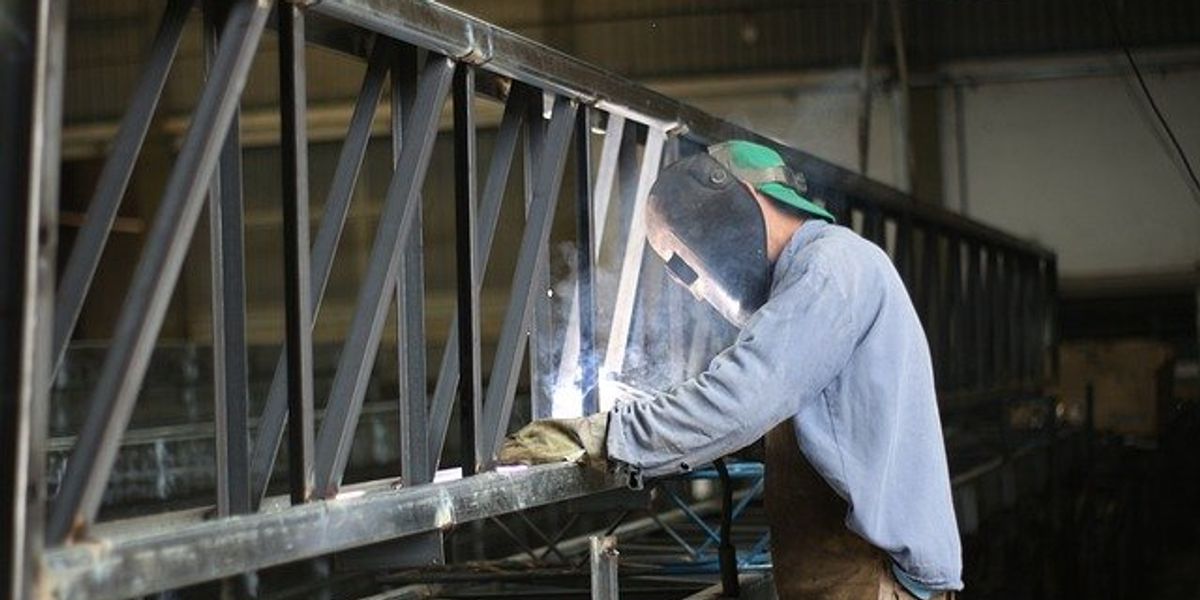 Welder with a face shield working on a steel beam in a warehouse.