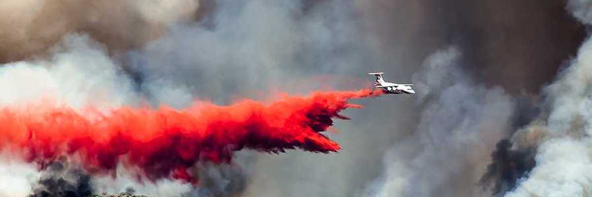 White aircraft dropping fire retardant as it battles the raging wildfire