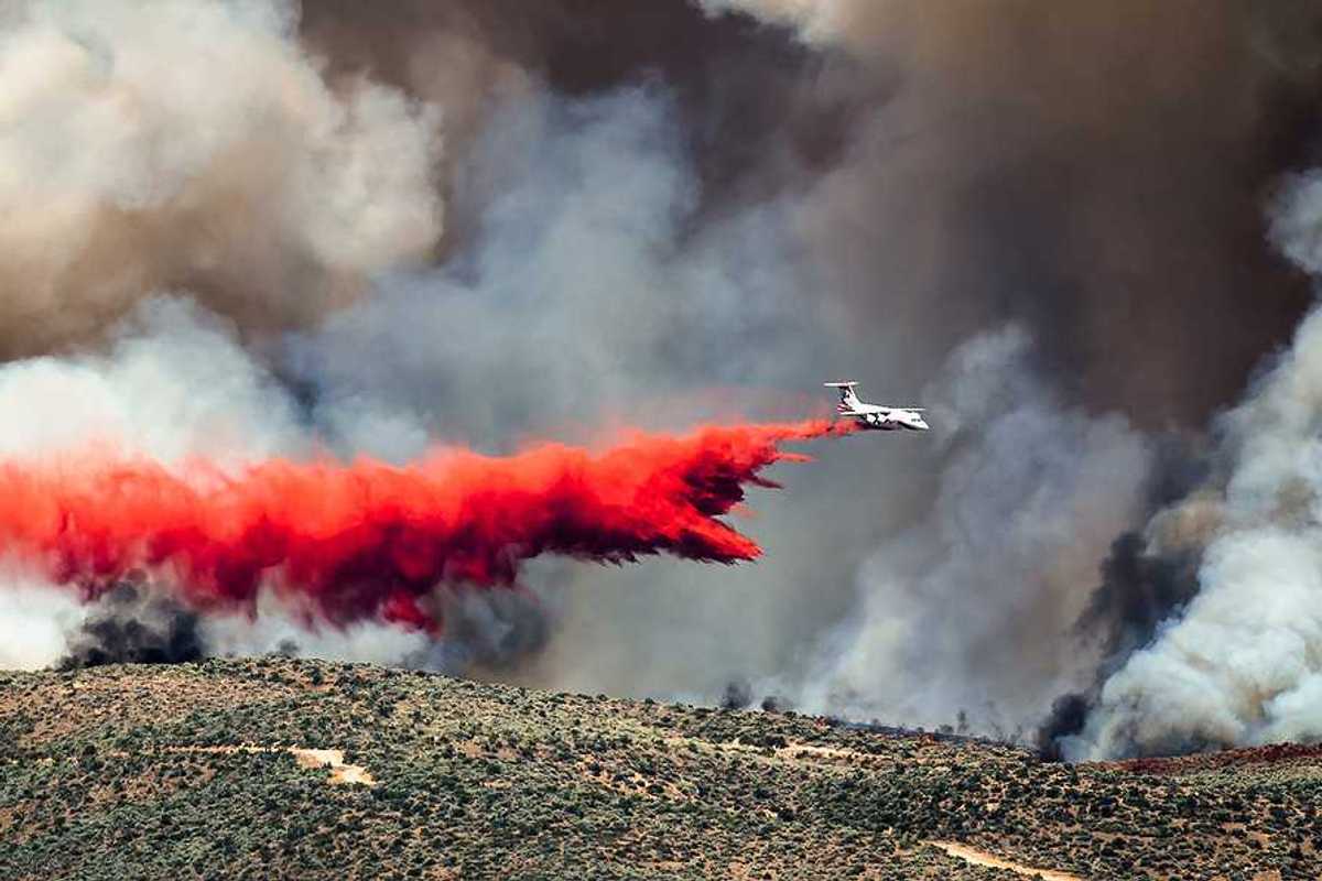 White aircraft dropping fire retardant as it battles the raging wildfire