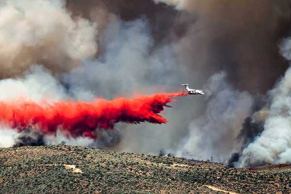 White aircraft dropping fire retardant as it battles the raging wildfire
