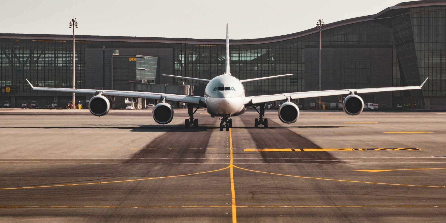 White airplane viewed from the front on the tarmac with an airport terminal in the background