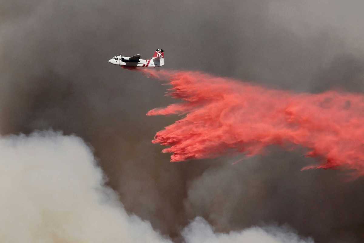 white and red airplane pouring red powder on fire with dark smoke in background.