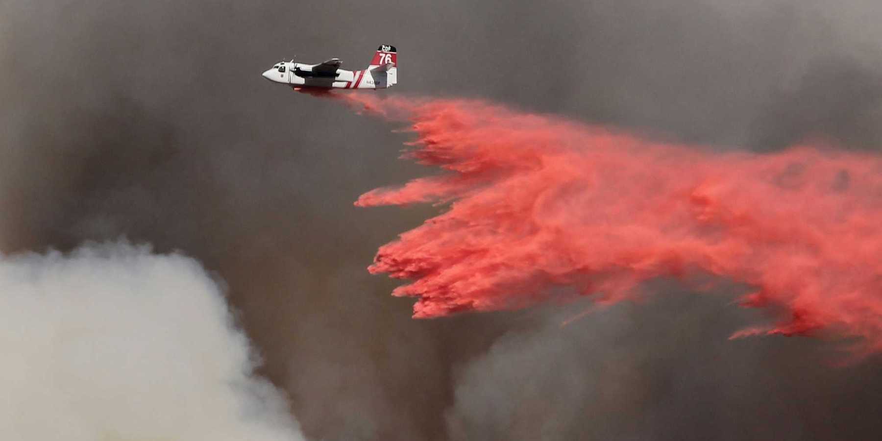 white and red airplane pouring red powder on fire with dark smoke in background.