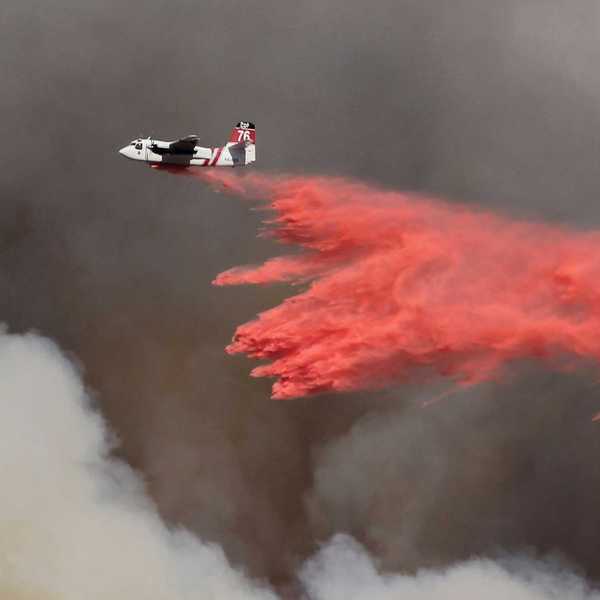 white and red airplane pouring red powder on fire with dark smoke in background.