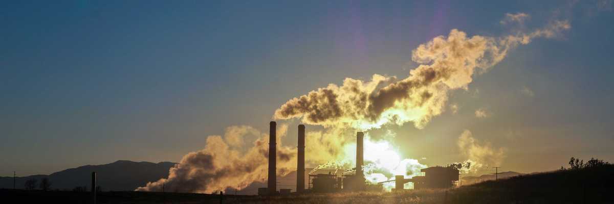 white pollution from smokestack billows over skyline during sunset.