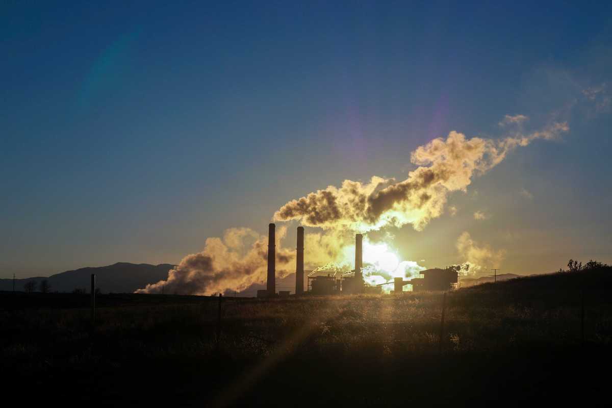 white pollution from smokestack billows over skyline during sunset.