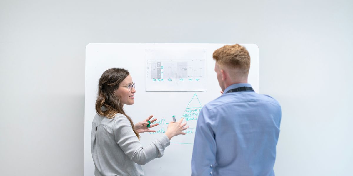 White woman explaining images on a whiteboard to a white man.