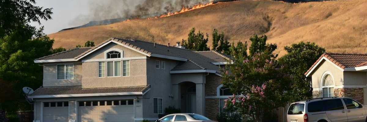 Wildfire on ridgetop threatens a neighborhood. Suburban home with vehicles in driveway.
