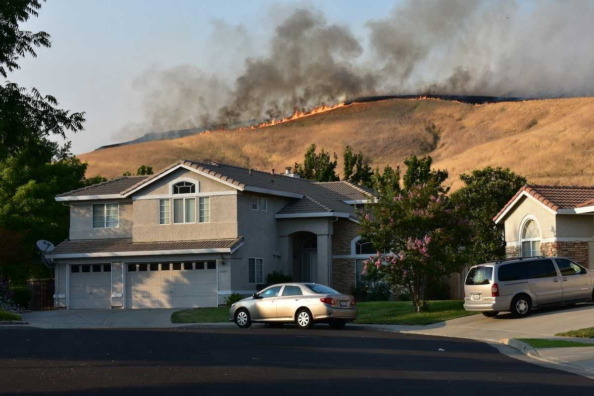 Wildfire on ridgetop threatens a neighborhood. Suburban home with vehicles in driveway.