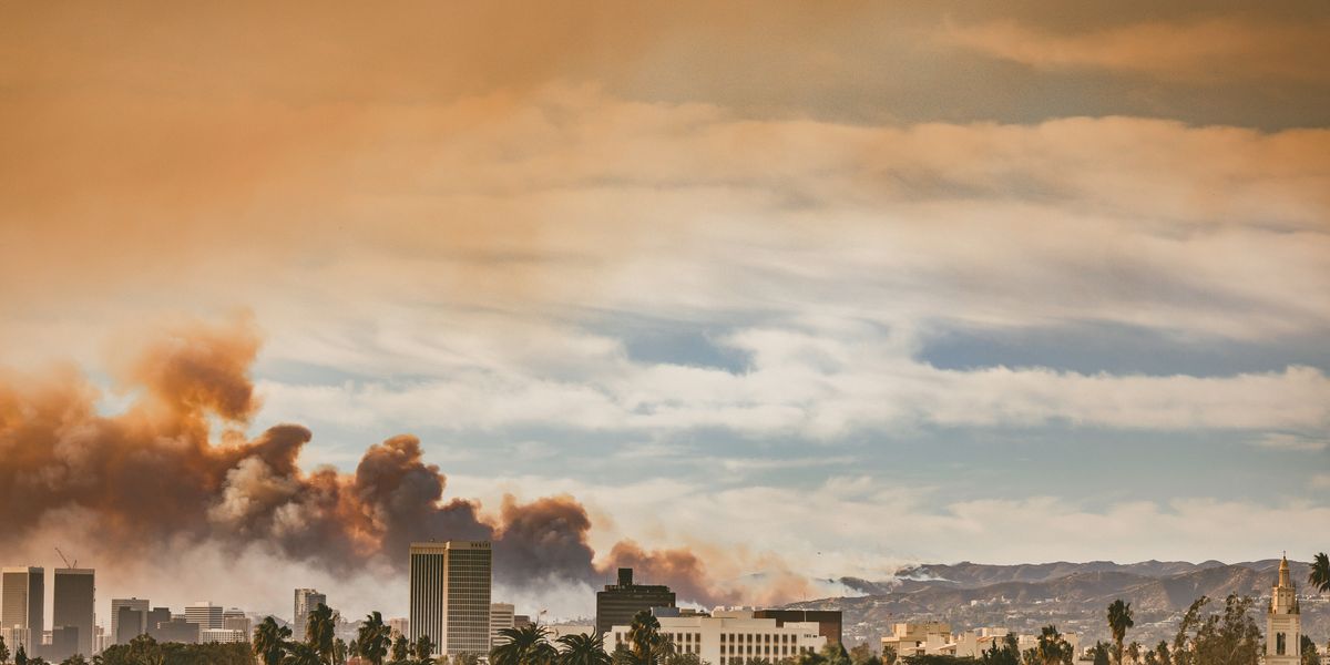 Wildfire smoke billows over Los Angeles with mountains in background.