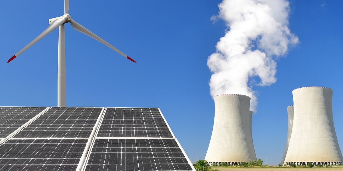 Wind turbine, solar panels and nuclear cooling towers with a blue sky in background.