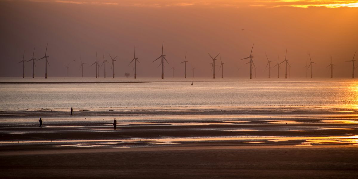 Wind turbines in the ocean in a row off a beach at sunset.