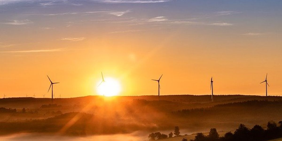 Wind turbines on a distant hill with the sun rising behind them.