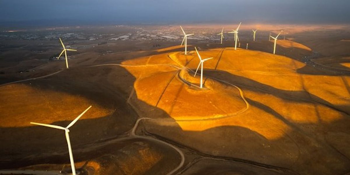 Wind turbines situated on dry hills above a valley.