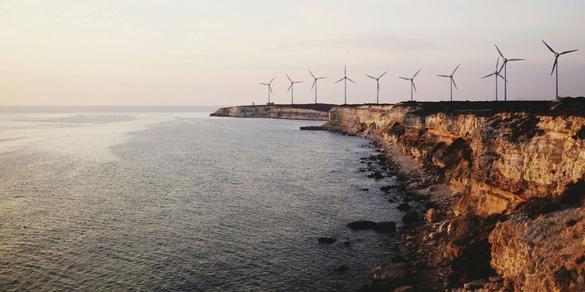 Windmills near rocky ocean cliffs.