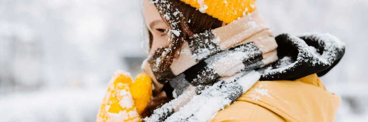 Woman bundled against cold, snowy weather wearing yellow coat andyellow hat.