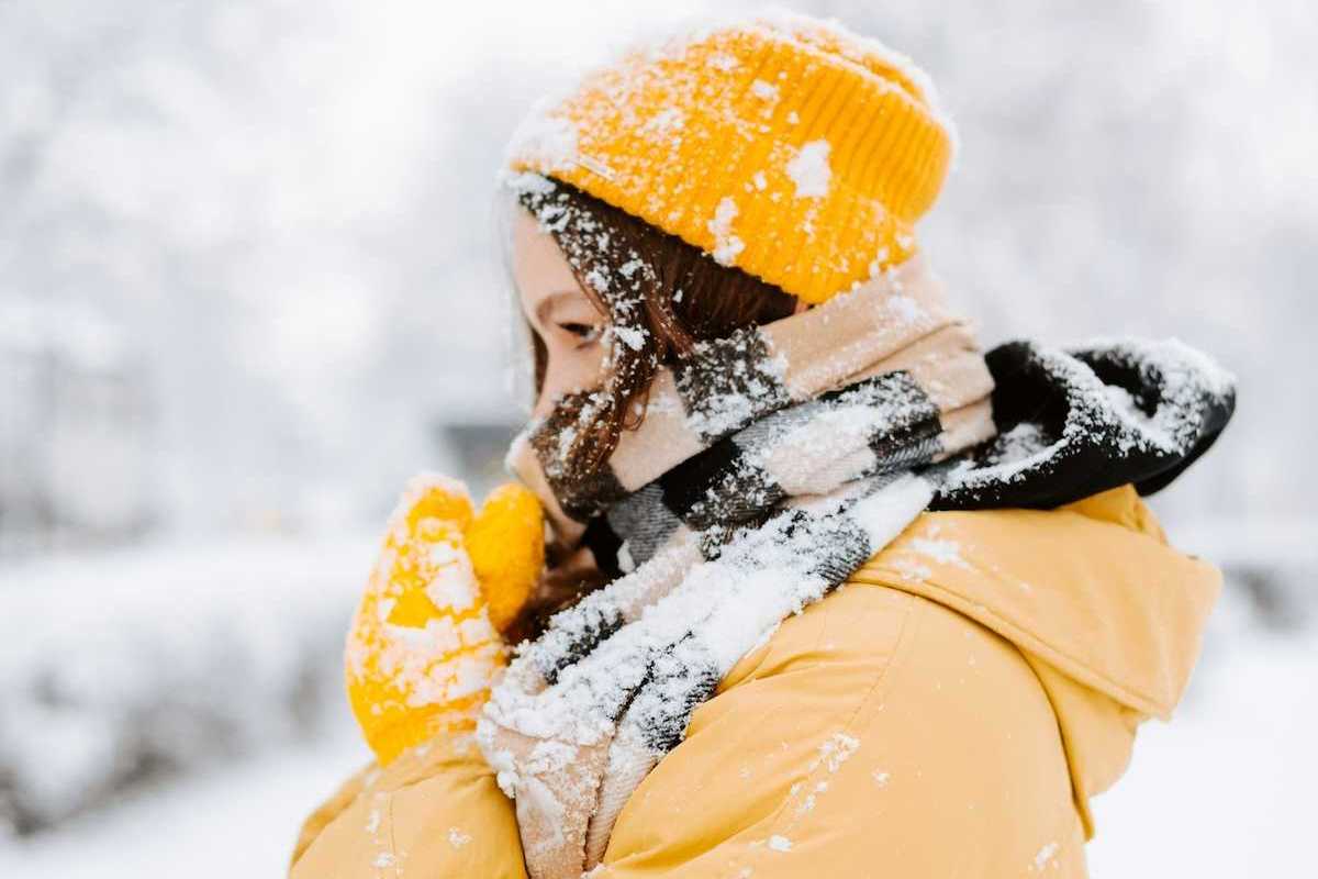 Woman bundled against cold, snowy weather wearing yellow coat andyellow hat.