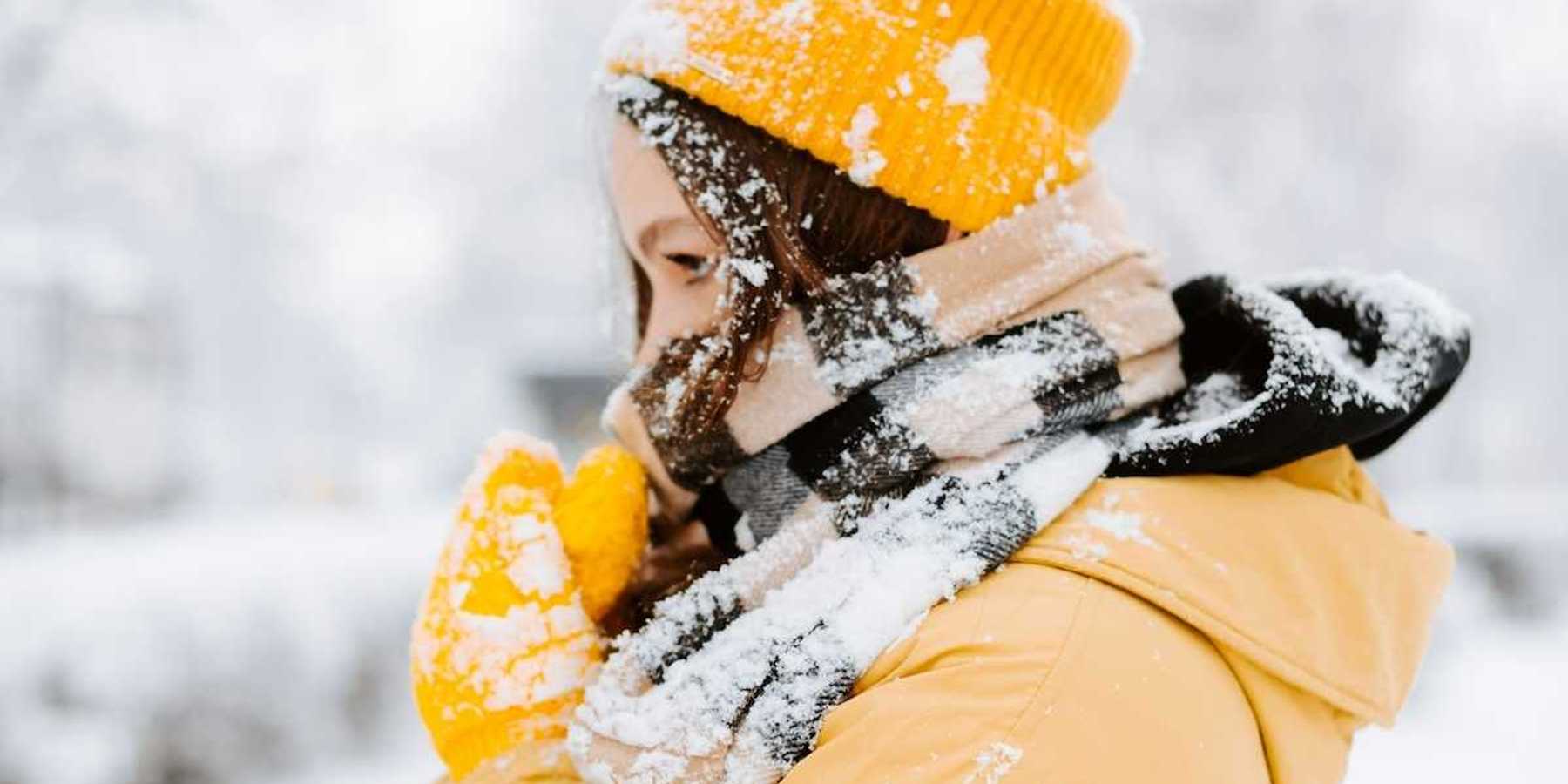 Woman bundled against cold, snowy weather wearing yellow coat andyellow hat.