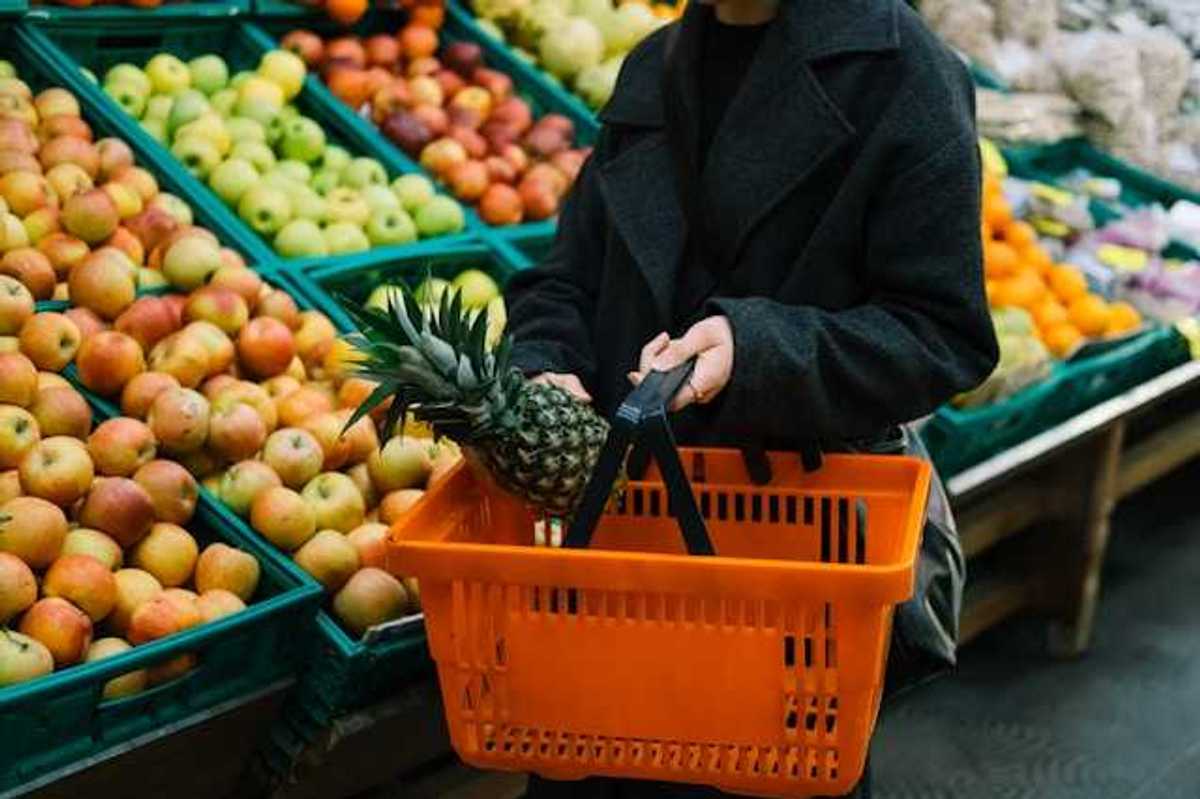 Woman carrying a hand cart in the vegetable and fruit section of a grocery store