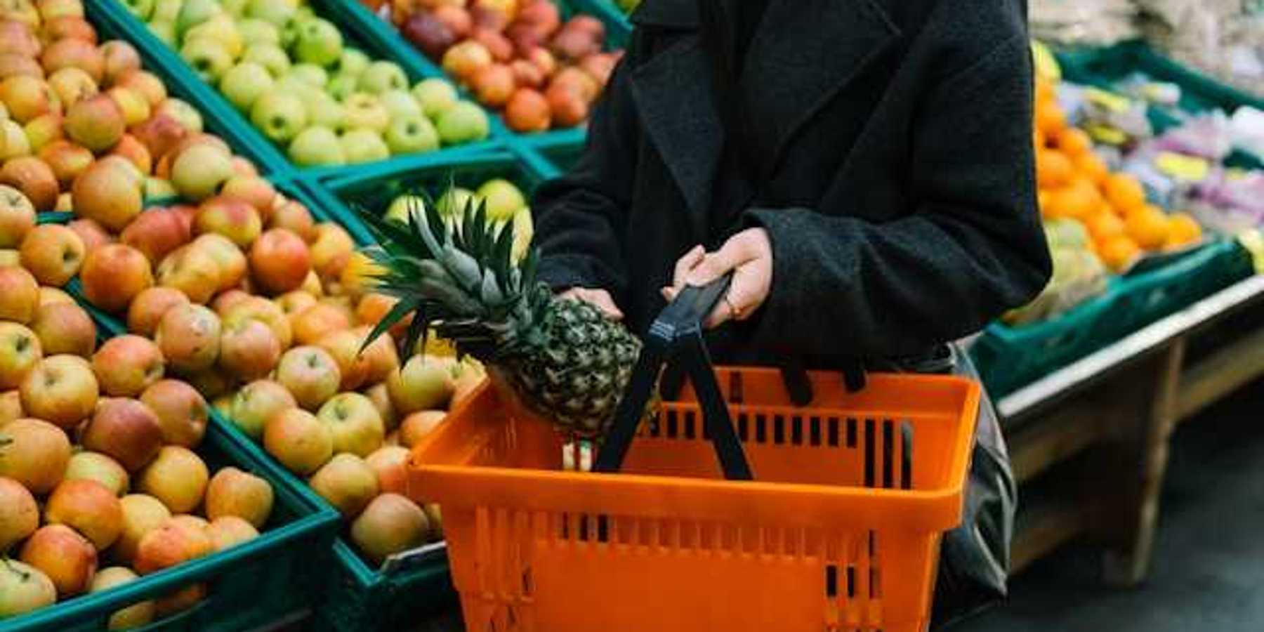 Woman carrying a hand cart in the vegetable and fruit section of a grocery store