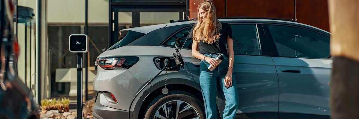 Woman dressed in blue jeans and black top casually charging an EV