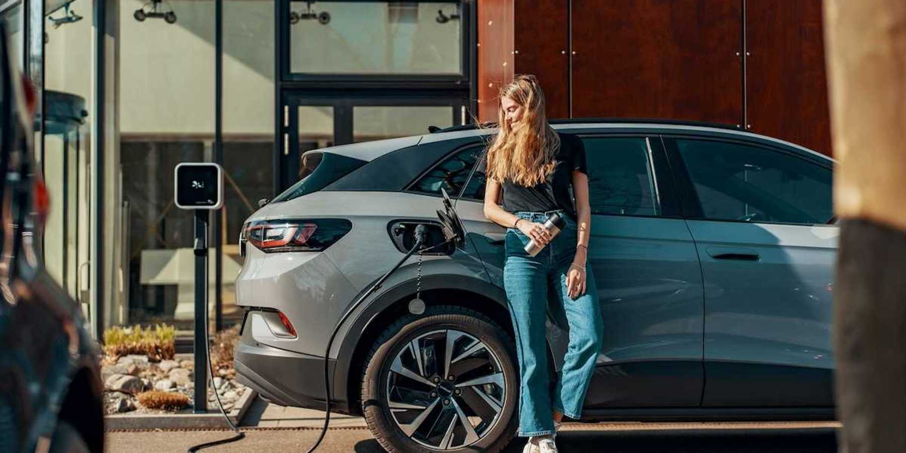 Woman dressed in blue jeans and black top casually charging an EV