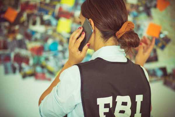 Woman FBI agent, back to camera, talking on the phone.