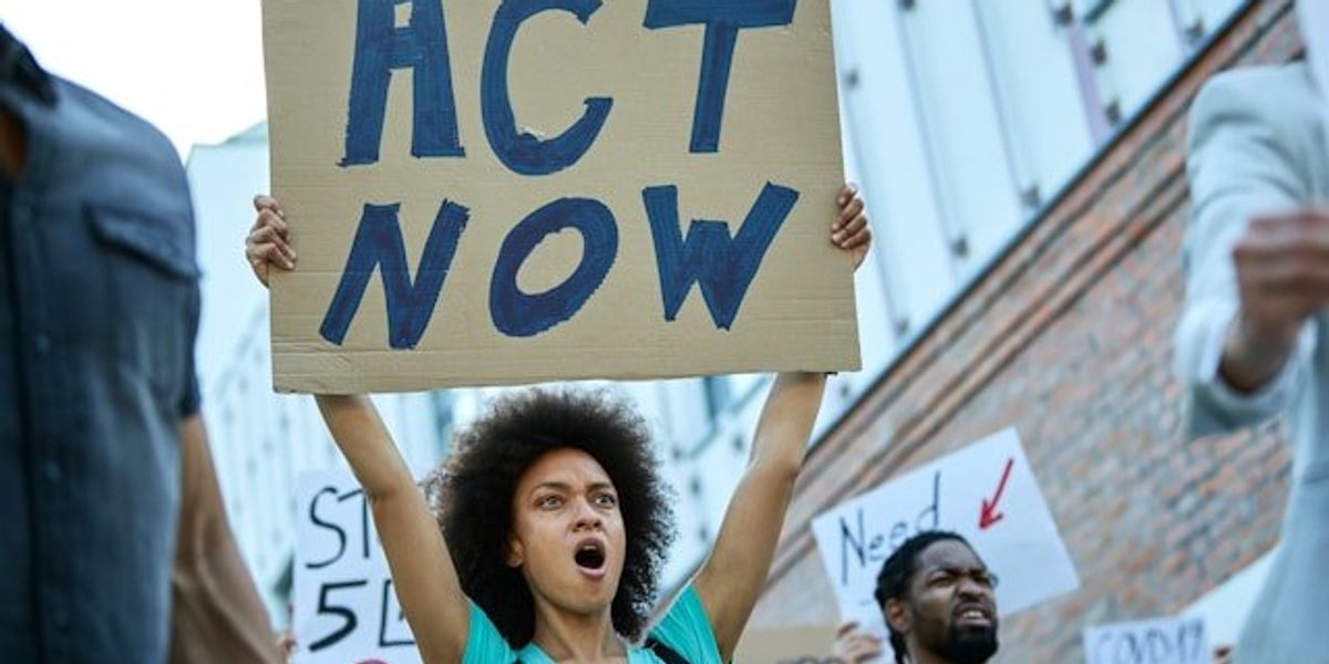 Woman holding a protest sign that says Act Now.