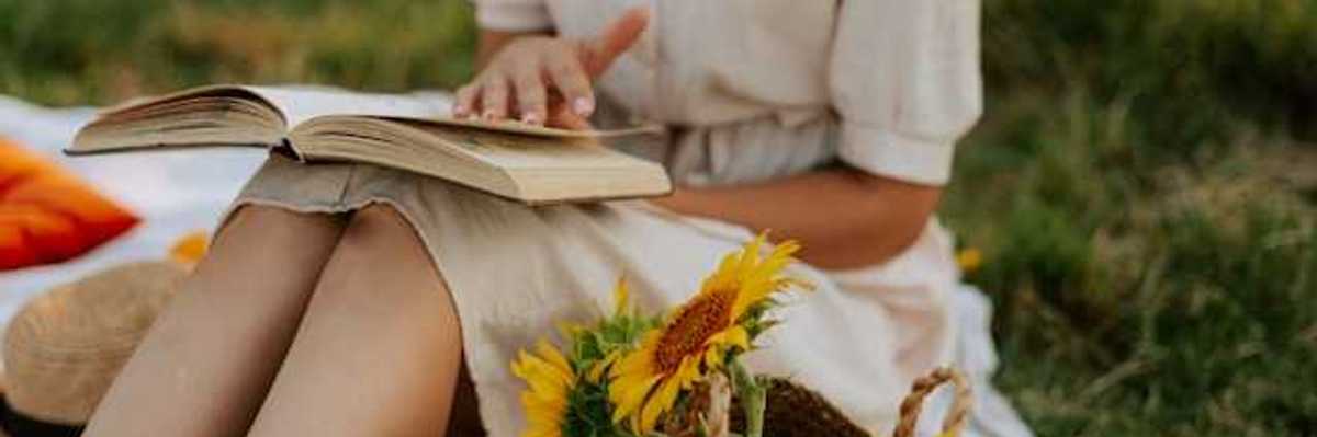 Woman in a summer dress reading a book next to a basket full of sunflowers