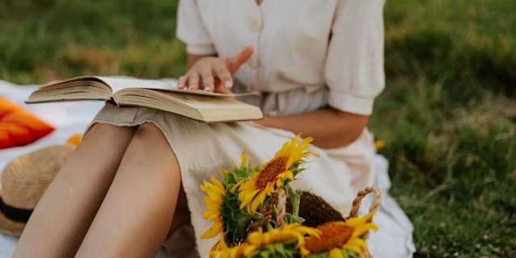Woman in a summer dress reading a book next to a basket full of sunflowers