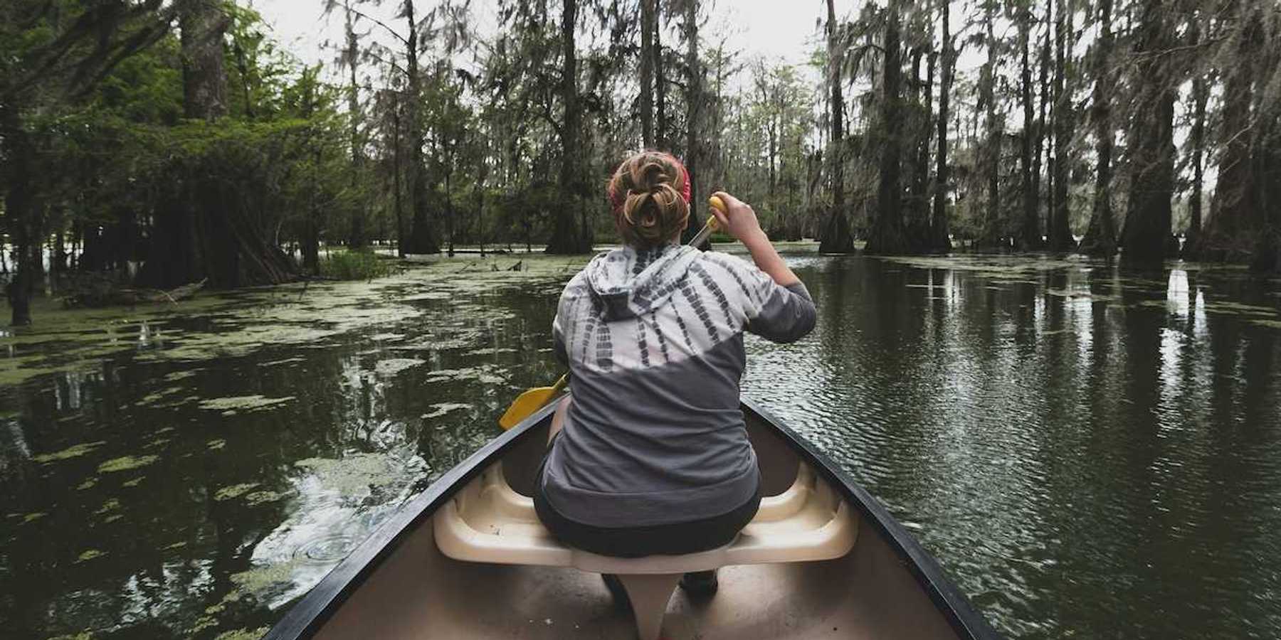 Woman in bow of canoe paddling in Bayou country shot from the stern of the canoe