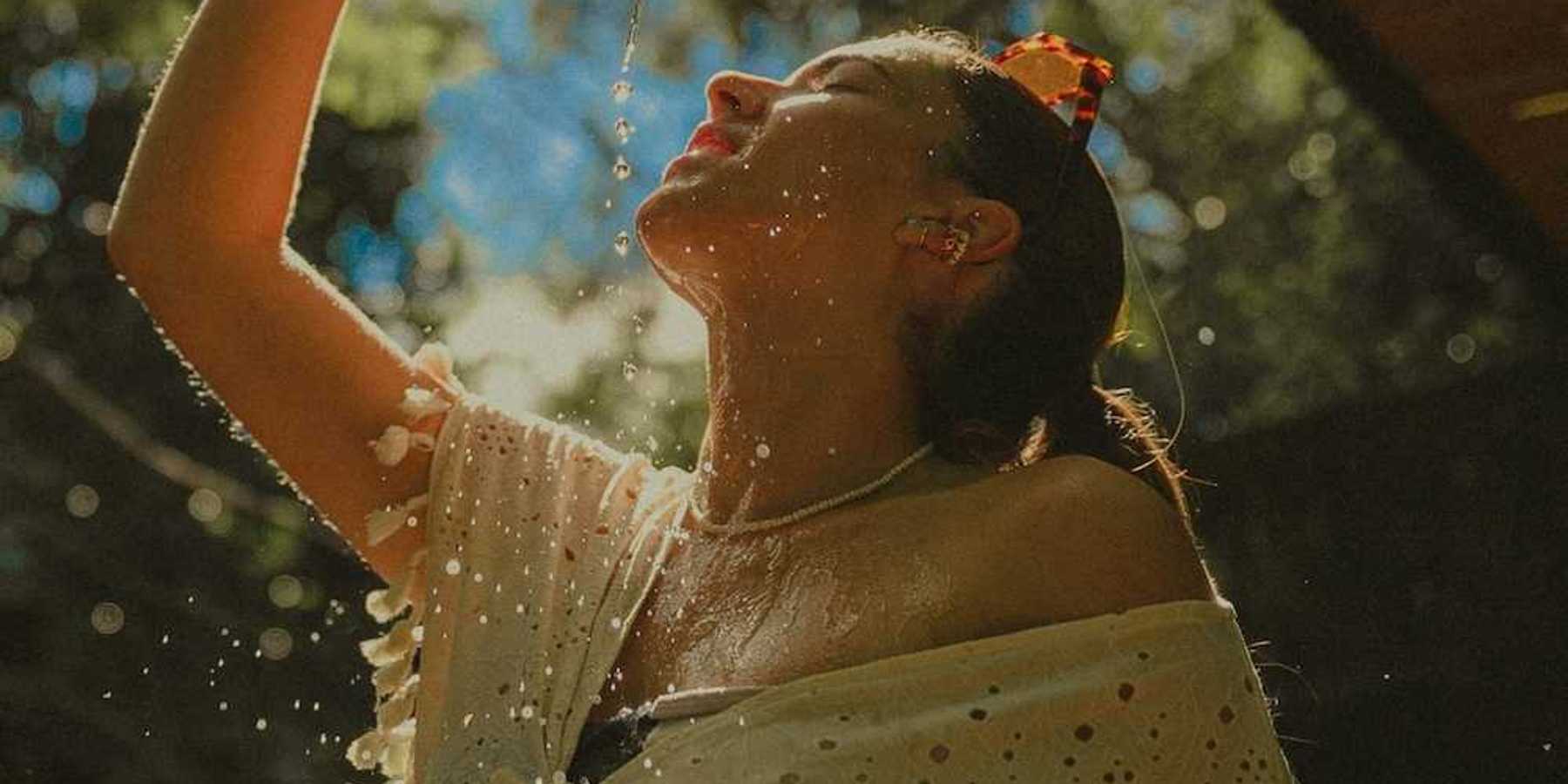 Woman in light clothing, cooling off by pouring water over herself.