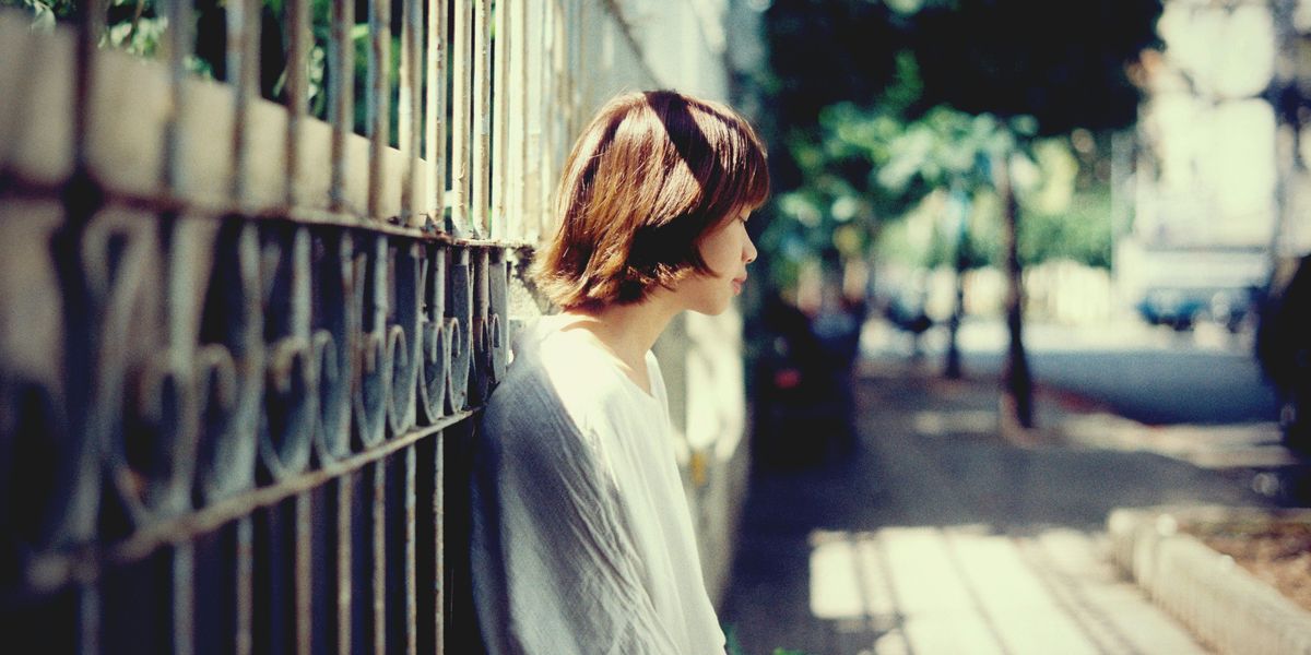 Woman leaning on a metal gate on a sunny day.