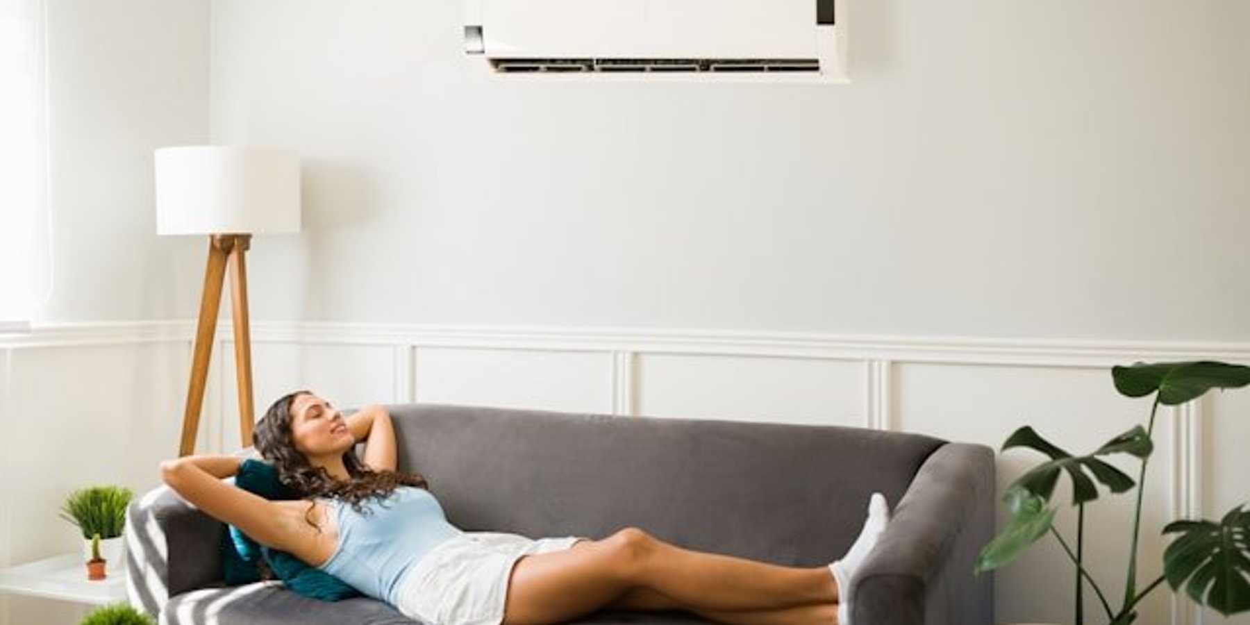 Woman lying on a sofa beneath a wall air conditioning unit