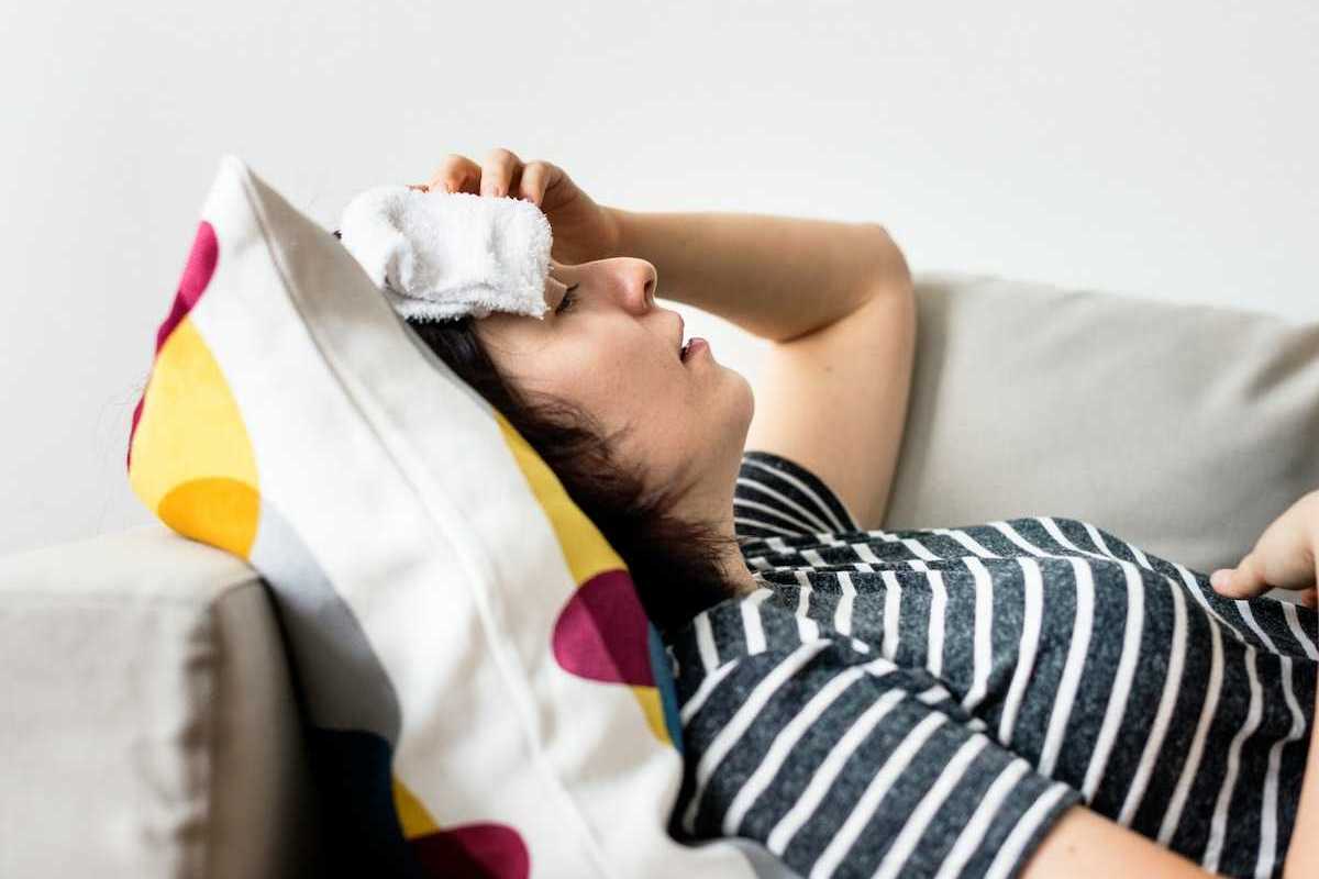 Woman, lying on a sofa with cold compress on forehead coping with extreme heat