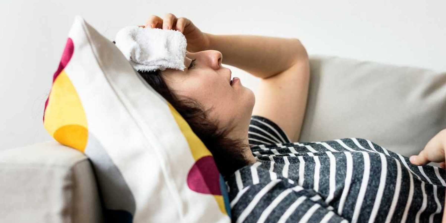 Woman, lying on a sofa with cold compress on forehead coping with extreme heat