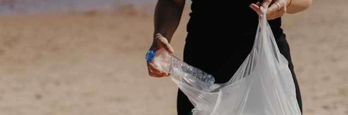 Woman placing a plastic bottle into a plastic bag on a beach