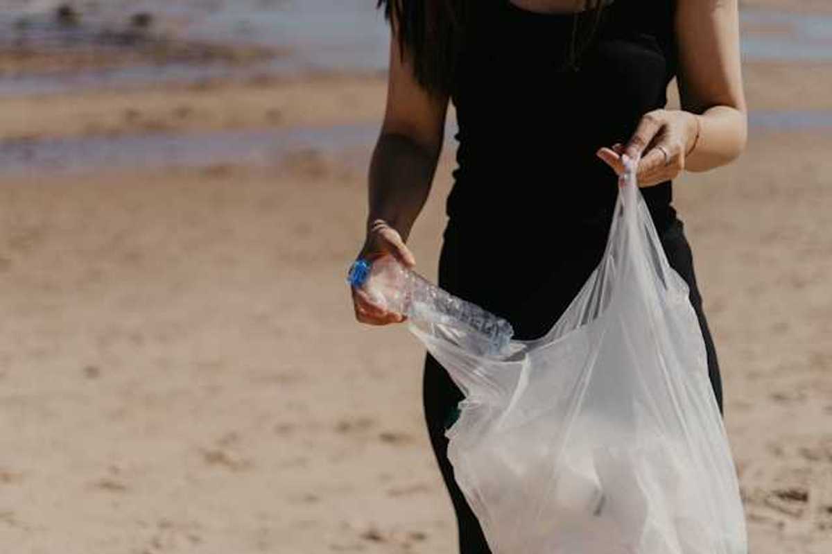 Woman placing a plastic bottle into a plastic bag on a beach