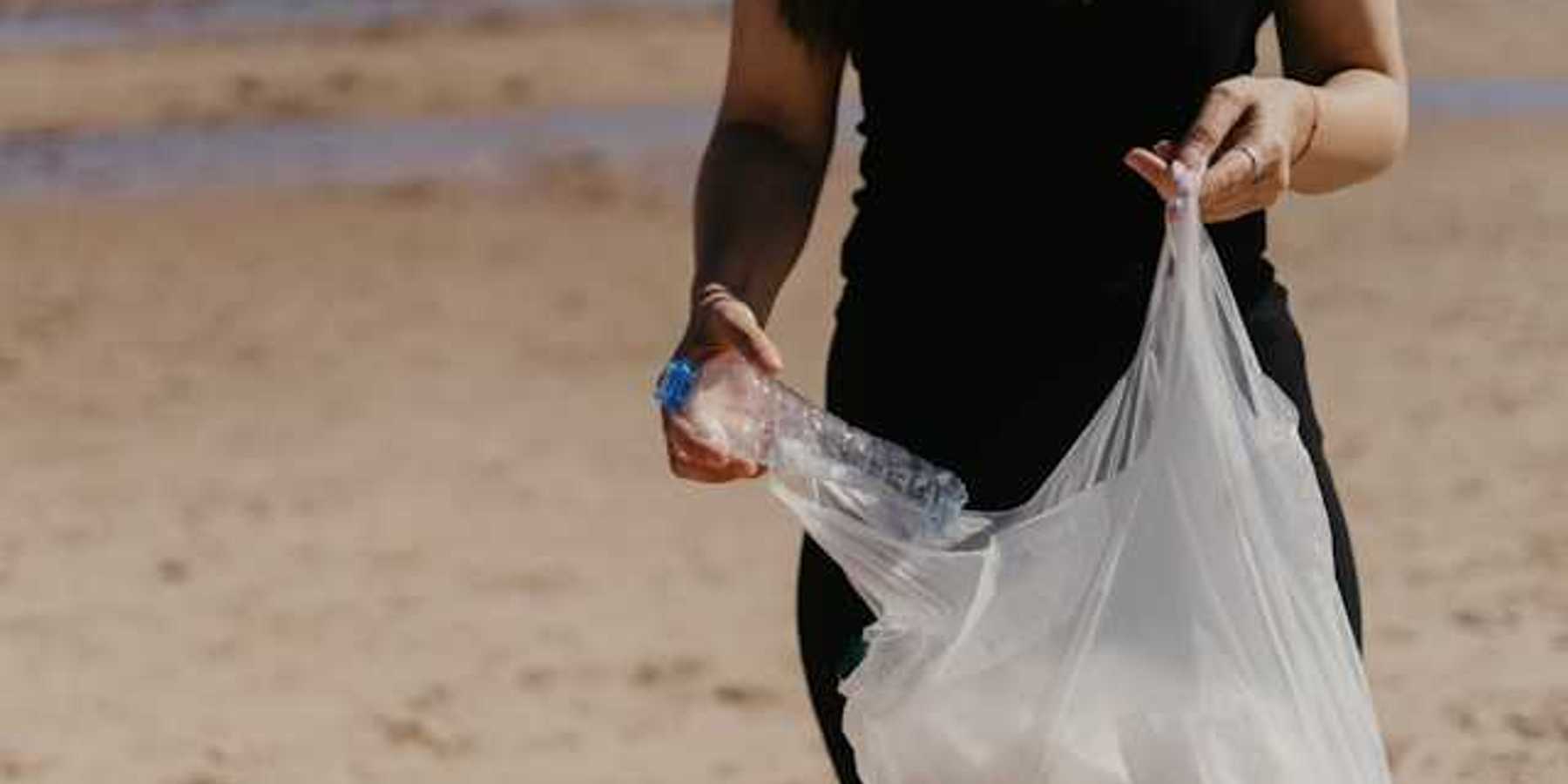 Woman placing a plastic bottle into a plastic bag on a beach