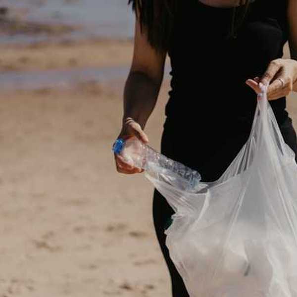 Woman placing a plastic bottle into a plastic bag on a beach
