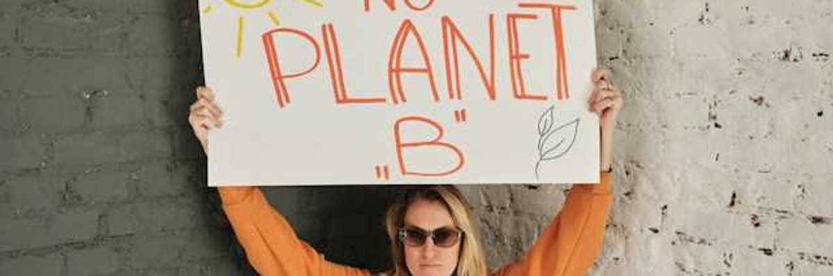 Woman wearing an orange sweatshirt holding a sign saying "There is no planet B"