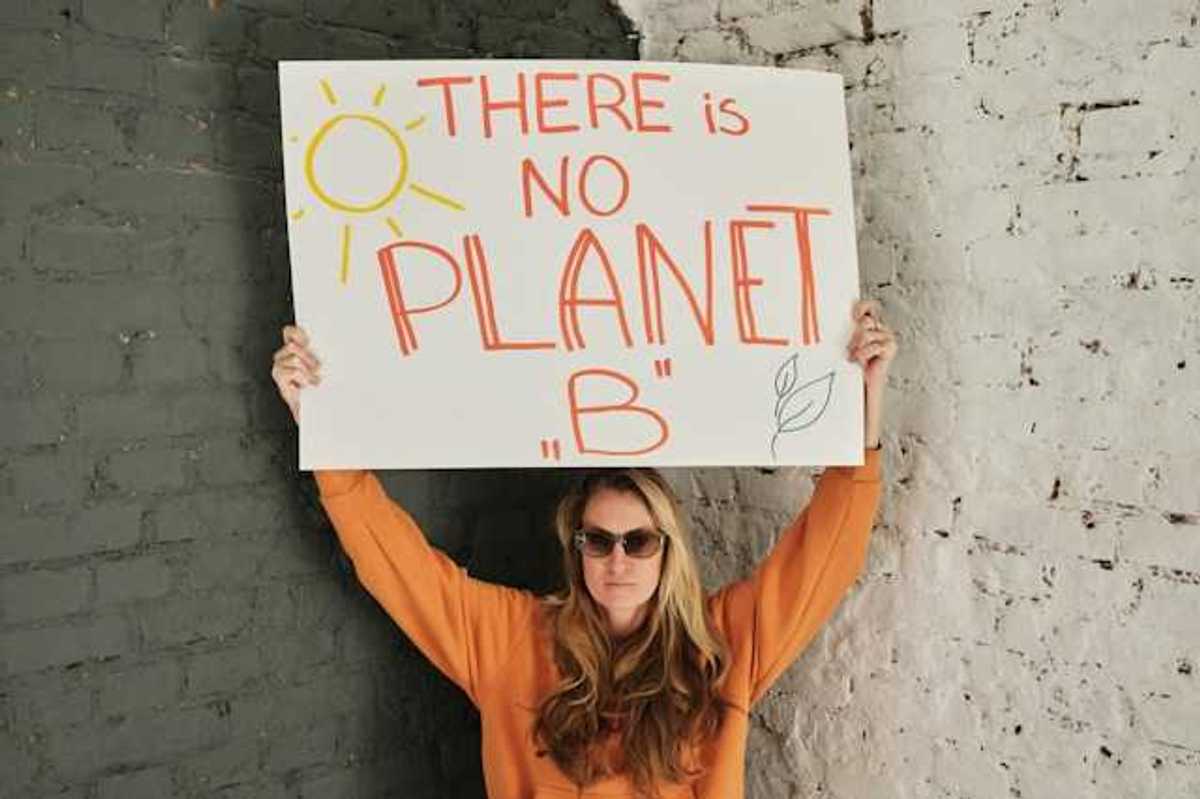 Woman wearing an orange sweatshirt holding a sign saying "There is no planet B"