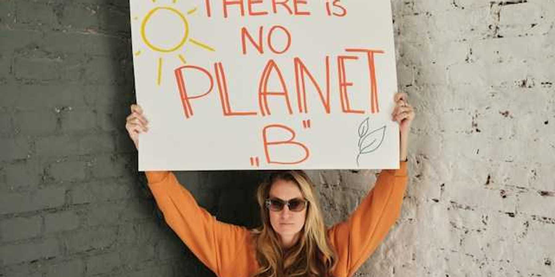 Woman wearing an orange sweatshirt holding a sign saying There is no planet B