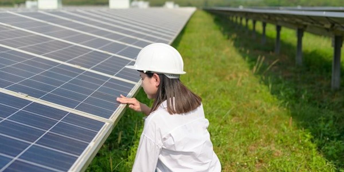 Woman wearing hard hat inspecting solar panels in a field.