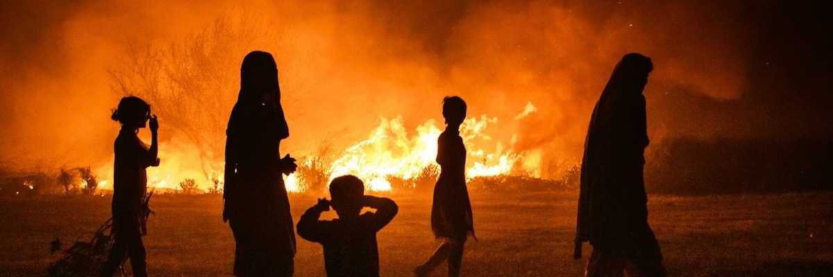 Women and children silhouetted against fire